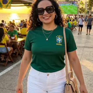 Mulher sorrindo vestindo uma blusa do Brasil feminina na cor verde com escudo e detalhes em amarelo, combinada com shorts branco. Produto da loja Leticy Moda Feminina.
